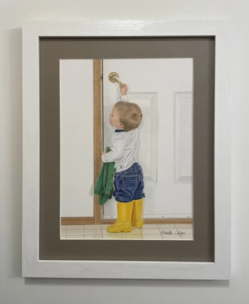 Framed and matted realistic drawing of a 2 year old boy with bright yellow rubber boots pulling down the handle to open a door to the outside. By Alberta artist Rochelle Colgan