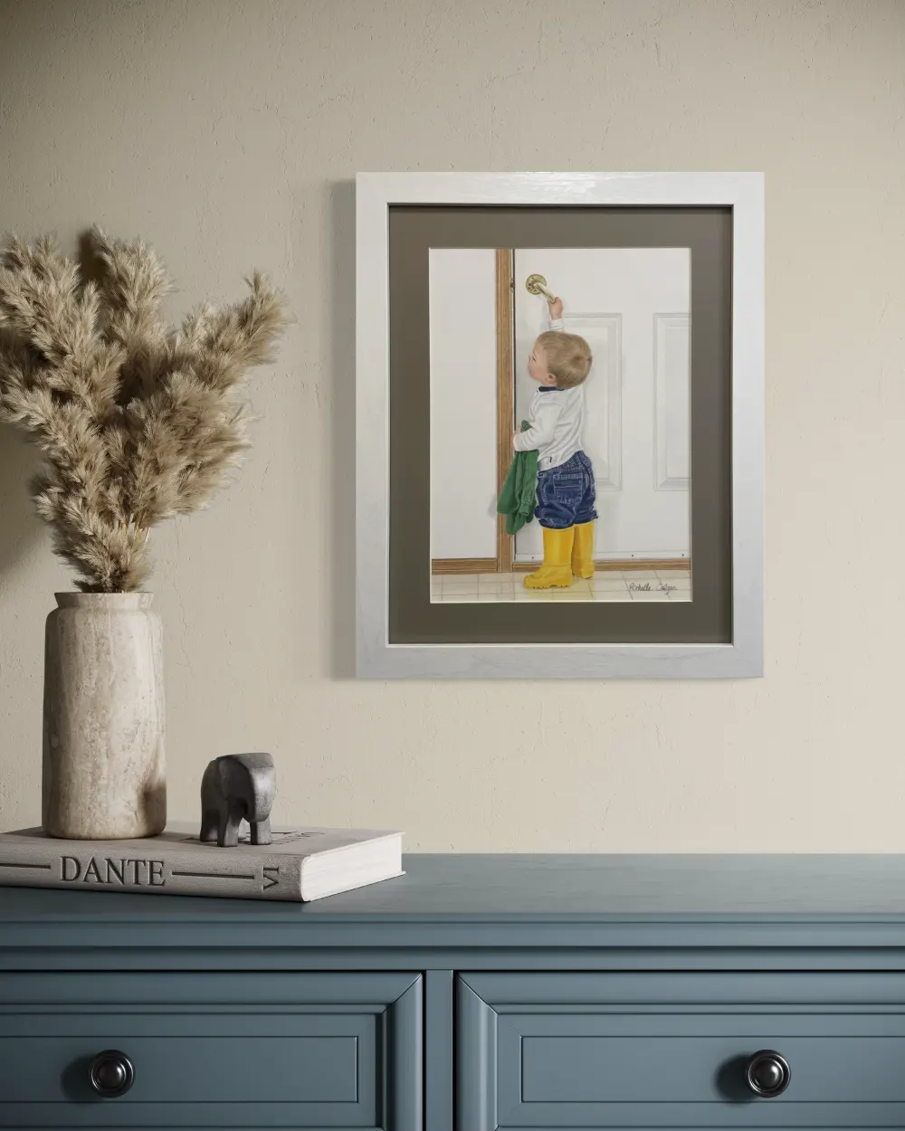 Framed realistic drawing of a 2 year old boy with bright yellow rubber boots pulling down the handle to open a door to the outside, hanging on a wall. By Alberta artist Rochelle Colgan