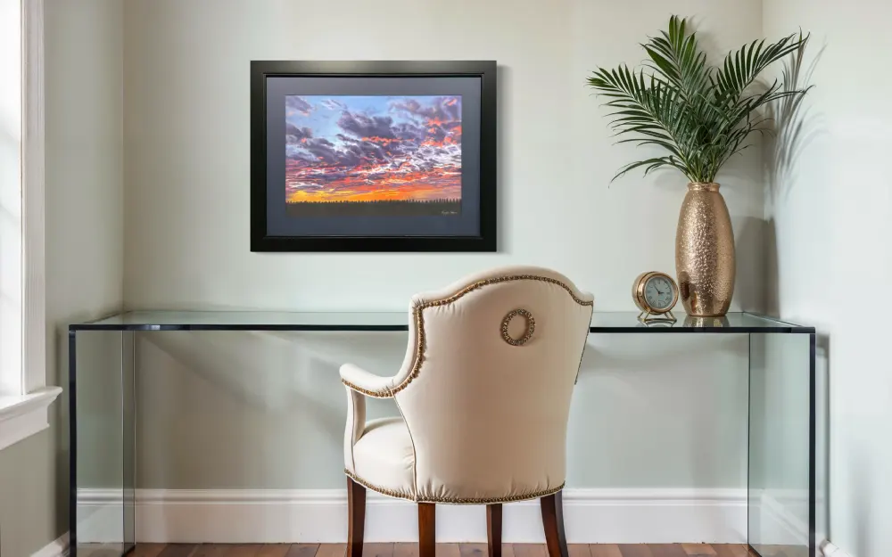 Framed realistic sunset skyscape drawing with purple, pink and orange clouds, light orange sky along the horizon with distant trees, hanging on a wall. By Alberta artist Rochelle Colgan