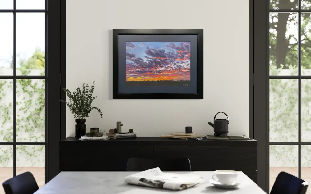 Framed realistic sunset skyscape drawing with purple, pink and orange clouds, light orange sky along the horizon with distant trees, hanging on a wall. By Alberta artist Rochelle Colgan