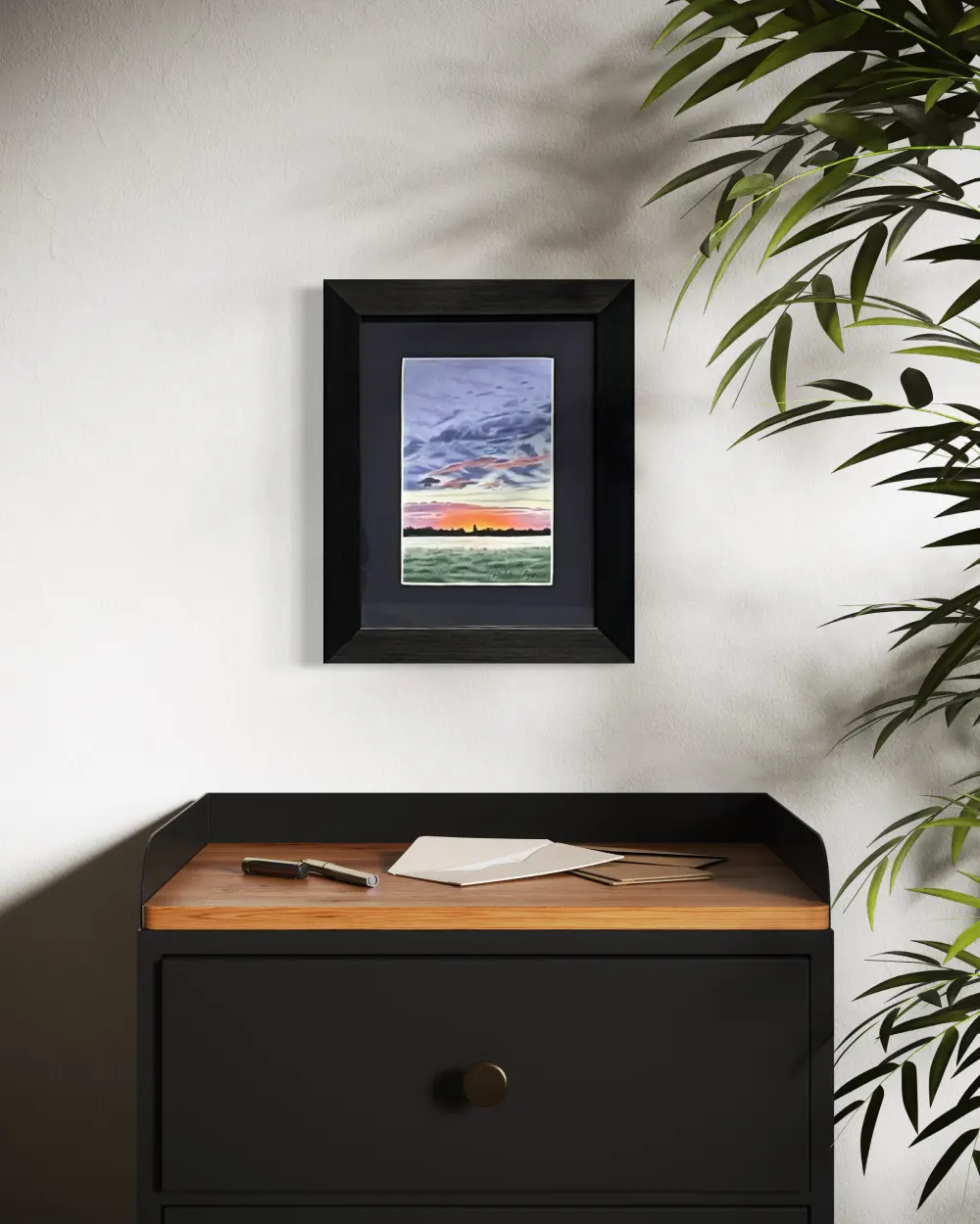 Framed realistic colourful sunrise skyscape drawing with dark clouds, purple and orange horizon, dark trees and mist over a lush green grass field, hanging on a wall. By Alberta artist Rochelle Colgan