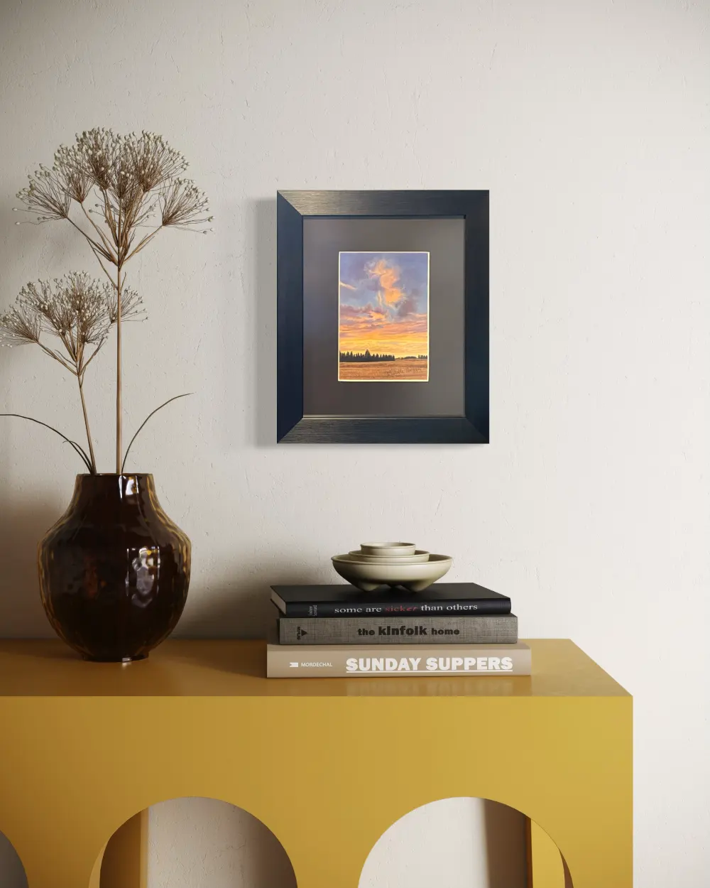 Framed realistic sunrise skyscape drawing of autumn crop field with trees along the horizon, hanging on a wall. By Alberta artist Rochelle Colgan