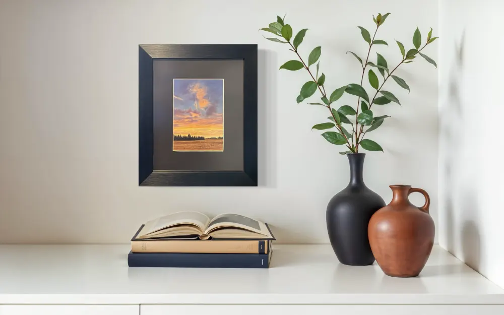 Framed realistic sunrise skyscape drawing of autumn crop field with trees along the horizon, hanging on a wall. By Alberta artist Rochelle Colgan