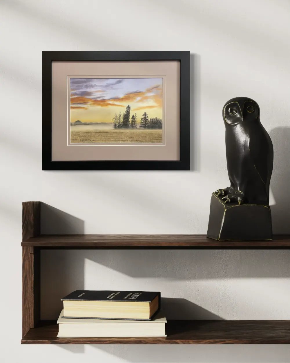 Framed realistic sunrise skyscape drawing with purple and orange clouds, light orange sky along the horizon with distant trees and mist, hanging on a wall. By Alberta artist Rochelle Colgan