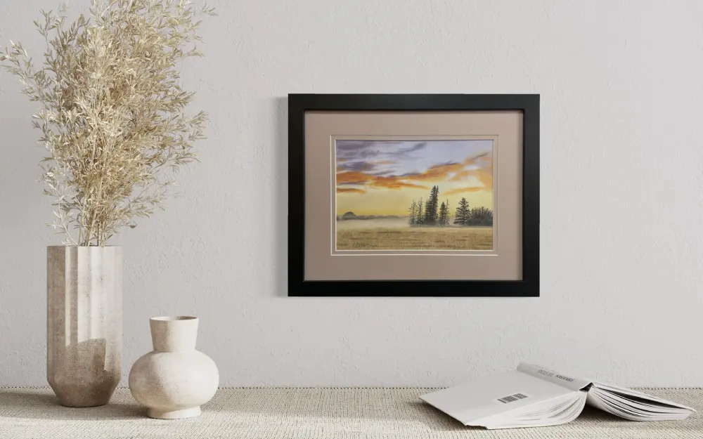 Framed realistic sunrise skyscape drawing with purple and orange clouds, light orange sky along the horizon with distant trees and mist, hanging on a wall. By Alberta artist Rochelle Colgan
