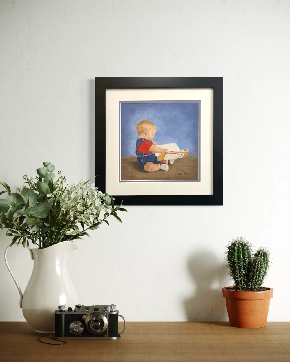 Framed realistic drawing of a 9 month old boy sitting on the floor looking at a story book, hanging on a wall. By Alberta artist Rochelle Colgan